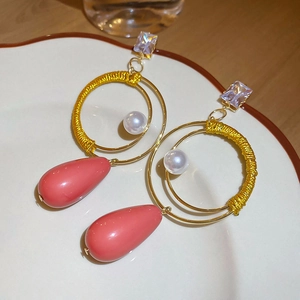 Dettaglio di orecchini boho con filo giallo intrecciato e ciondolo a goccia rosa