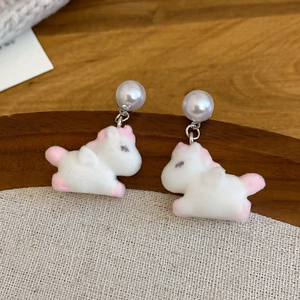 Close-up of cute flocked unicorn earrings with faux pearls on a textured beige tray
