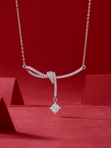 Macro view of silver bow necklace with princess cut gemstone and red geometric background