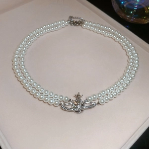 Detailed macro view of double-layer pearl necklace with a crystal-encrusted Saturn pendant
