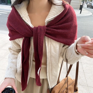 Detail eines burgunderroten Strickschals, geknotet über einem weißen Strickkardigan