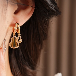 Detail of model wearing gold double gourd earrings with tiger eye stone and zircons