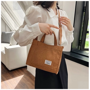 Detail of a brown corduroy tote bag featuring a white woven label and adjustable shoulder strap