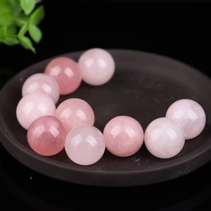 Natural pink quartz polished round beads displayed on a dark tray with a green leaf accent