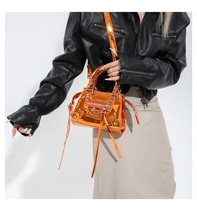 Detail of metallic orange crossbody bag with silver studs and long tassels on black jacket