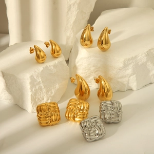 Gros plan de boucles d'oreilles goutte dorées et clous carrés sur pierre blanche