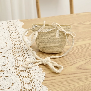 Close-up of girls' straw crossbody bag with white lace bows and woven strap detail