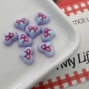 Macro shot of 8/10mm resin heart nail charms with pink bows on a ceramic plate