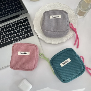 Detailed texture of corduroy makeup pouches in grey, pink, and dark green on a desk