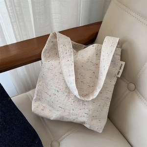 Detail of off-white canvas tote bag with color speckles on a leather chair