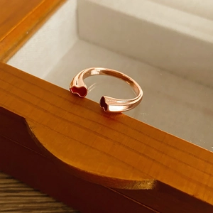 Gros plan sur une bague ouverte en or rose avec deux breloques cœurs rouges et boîte