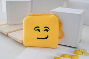 Detail of yellow plush coin purse with embroidered smirk face and plastic hook attachment