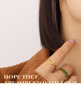 Detail of stacked gold rings with emerald green stones and geometric tassel earrings