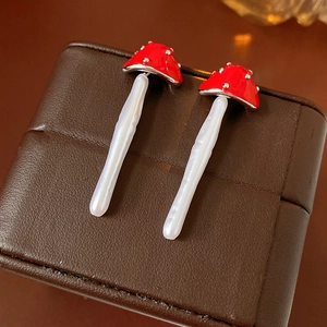 Close-up of red mushroom earrings with white dots on a brown leather jewelry box