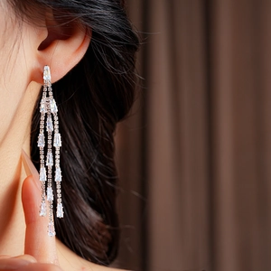 Close-up of silver triangle tassel earrings with sparkling rectangular crystals on a model