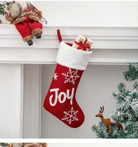 Detail of red knit Christmas stocking with white Joy embroidery hanging on a fireplace
