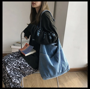 Detail of a large washed denim tote bag with side pockets on a casual model