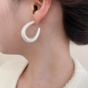 Close-up of minimalist white C-shaped acrylic hoop earrings on model with pearly finish