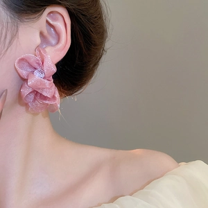 Macro detail of a soft pink chiffon flower earring worn by a model in natural light