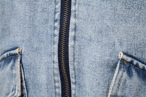 Macro shot of vintage brass zipper and stitching on washed blue denim jacket