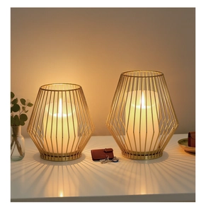 Close-up of geometric gold iron lanterns with glowing LED candles on a white surface