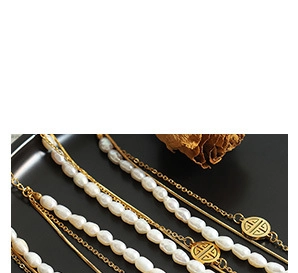 Detailed close-up of layered baroque pearl necklace with golden geometric charm on dark stand