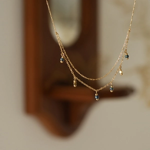 Detailed close-up of double-layer gold chain necklace with vintage blue beads and pendants
