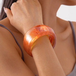 Detail of amber acrylic wide wave bangle showing natural marbled texture and translucent finish