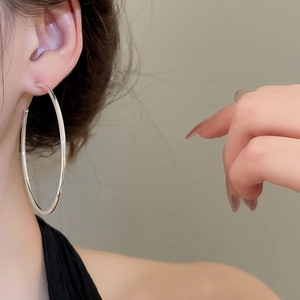 Detail view of large silver geometric C-shaped earrings worn by a model in soft light