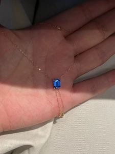Gros plan d'un collier doré avec une pierre bleue taille émeraude tenu à la main