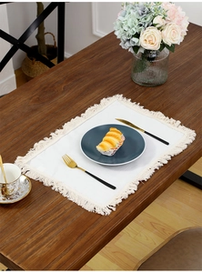 Detail of bohemian cotton linen placemat with fringe on a rustic wooden table