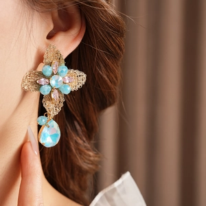 Detail of vintage gold wire cross earring with blue and purple crystals on model