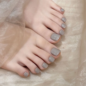 Elegant Morandi grey press-on toenails with glossy finish on a champagne fabric background