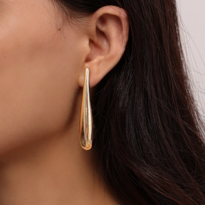 Detailed close-up of long golden teardrop earrings with a high-polished mirror finish