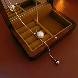 Detail of silver snake chain necklace with pearl pendant on a wooden jewelry box