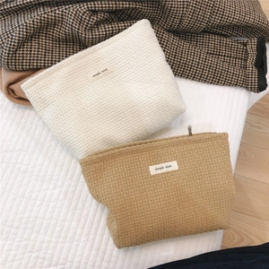 Close-up of woven cosmetic bags in off-white and camel with simple wish labels