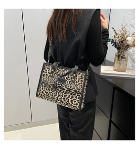 Modern leopard print tote bag with black leather trim shown on model's shoulder