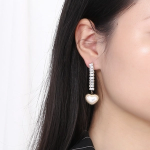 Close-up of long tassel earrings with sparkling rhinestones and a heart-shaped pearl pendant