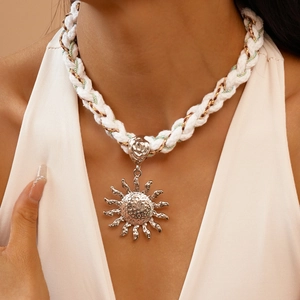 Close-up of a large silver sun pendant on a chunky white braided rope necklace cord