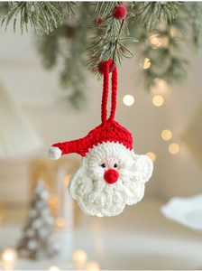 Close-up of handmade knitted Santa ornament hanging on pine branches with bokeh lights