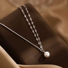 Macro view of silver layered snake chain necklaces featuring a round white pearl pendant
