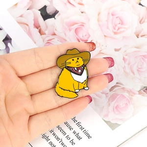 Macro view of a cute enamel cat pin wearing a cowboy hat and red bandana on a hand
