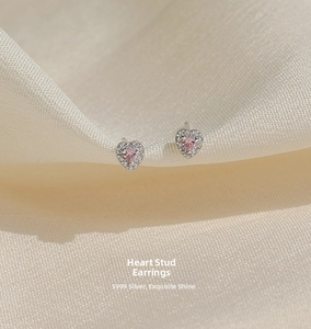Macro detail of S999 silver heart stud earrings with pink gemstone on satin fabric