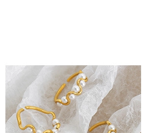 Macro shot of gold-plated wavy open ring with five white pearls on white fabric