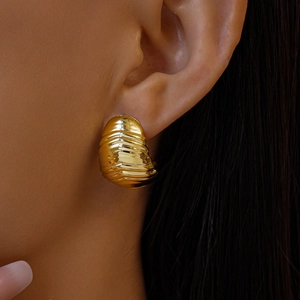 Gros plan de grandes boucles d'oreilles dorées à texture ondulée sur un mannequin