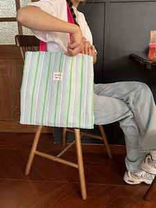 Borsa tote a righe con manici rosa e logo del marchio in un ambiente di caffè accogliente