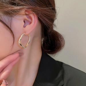 Detail of twisted geometric gold hoop earrings with inset diamonds worn by model