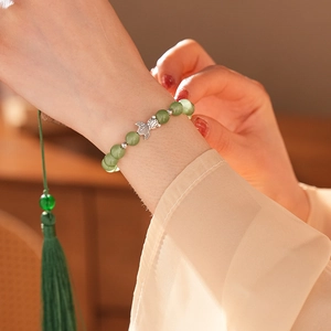Detail of green jade beads bracelet featuring a silver fish pendant and green silk tassel