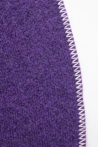 Dettaglio macro del tessuto in pile viola con cuciture a zigzag a contrasto sul bordo