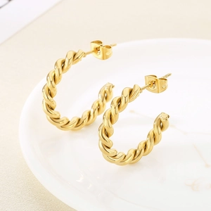 Détail macro de boucles d'oreilles créoles dorées torsadées en C au fini métallique